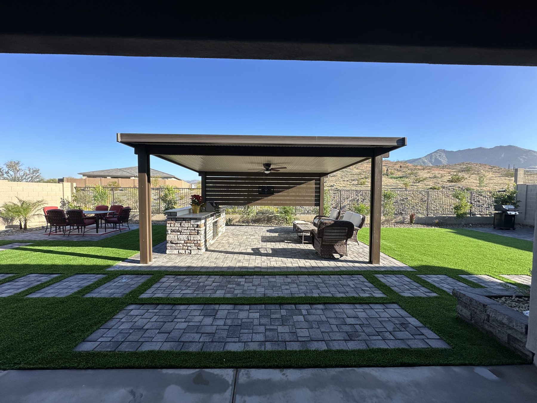 Backyard with a dark steel pergola, paver patio and artificial turf, mountains in the distance