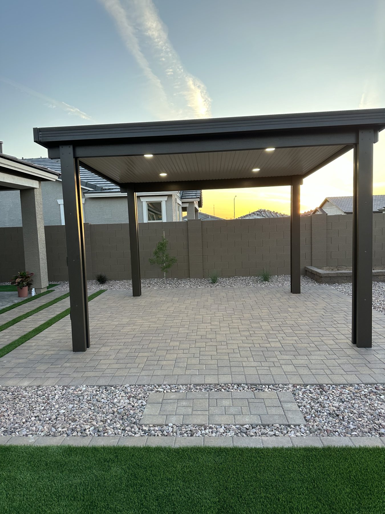 Steel pergola with recessed lights over a paver patio at sunset